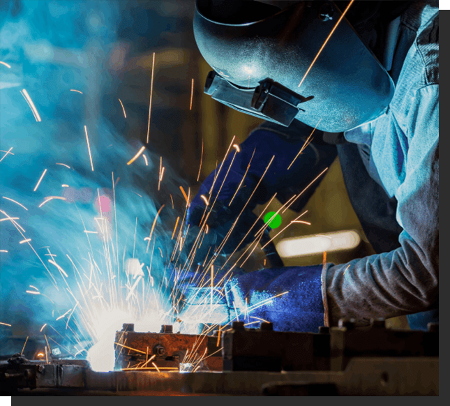 A person welding in the middle of a factory.